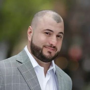 Man with short hair and beard in gray checkered suit.