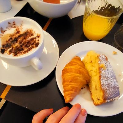 A breakfast plate with croissant, cake slice, cappuccino, and orange juice.