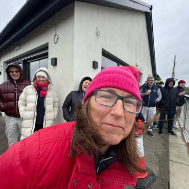 A woman in a pink hat smiles close to the camera with a group of people behind her outdoors.