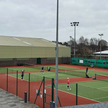 People playing tennis on outdoor courts on a cloudy day.