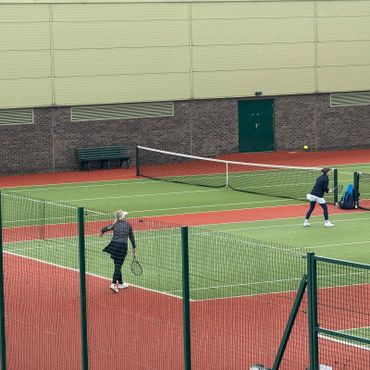 Two people playing tennis on an outdoor court with a green and red surface.