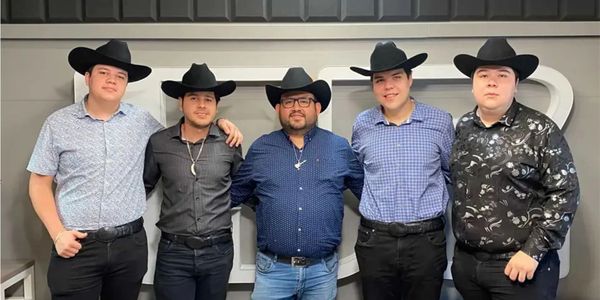 Five men wearing cowboy hats and patterned shirts posing together indoors.