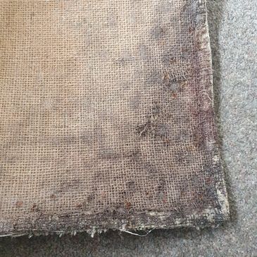 Worn, frayed burlap sack corner on a carpeted floor.