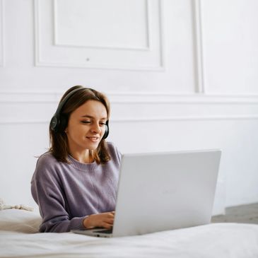 A young woman wearing headphones, engaging online. Looking related and calm. 