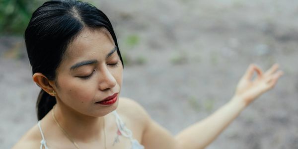 A woman with closed eyes meditates outdoors with a serene expression.