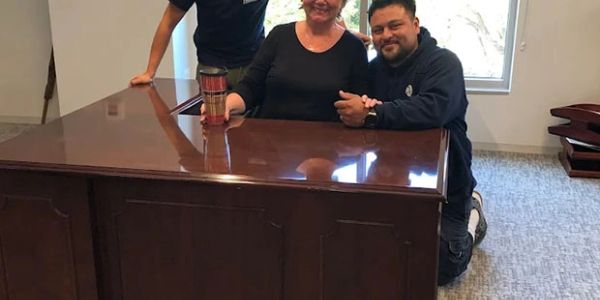 Three people smiling around a wooden desk with a coffee cup.