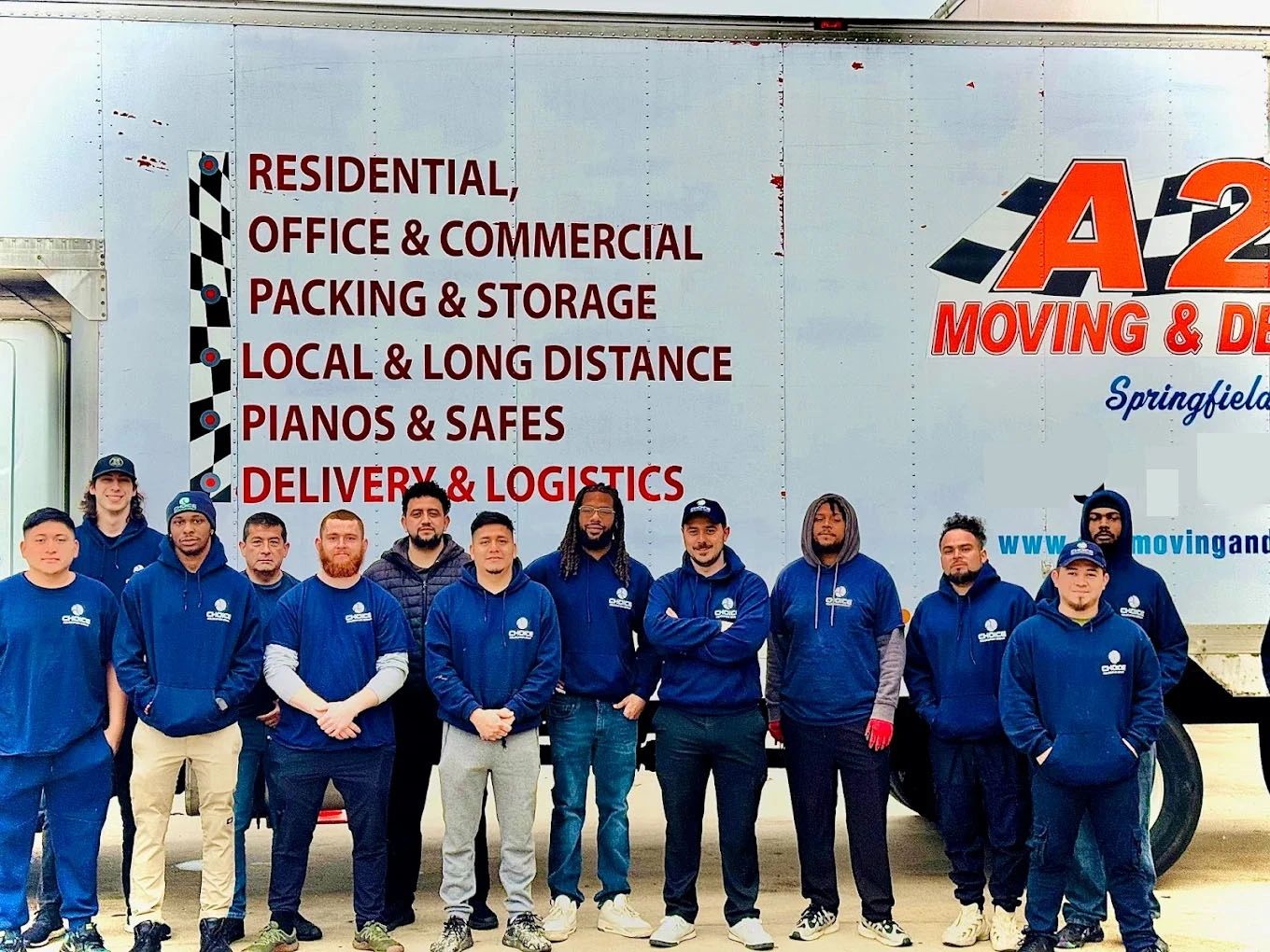 Group of movers in blue uniforms posing in front of a moving truck.