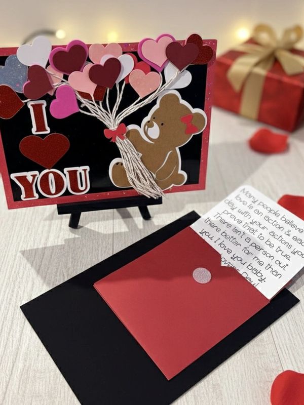 A cute teddy holding heart balloons with an 'I love you' message and a handwritten note.