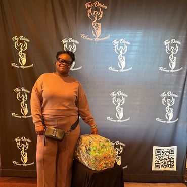 Woman posing beside a colorful backpack at The Divine Women Movement event.