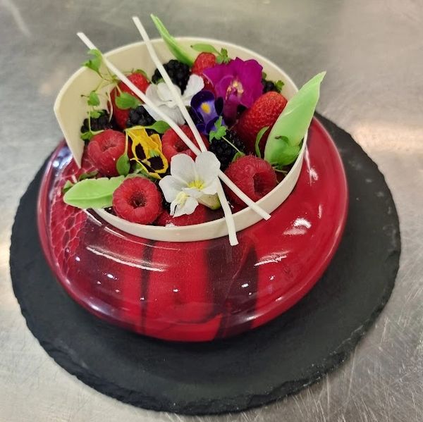 A vibrant red and black dessert topped with fresh berries and edible flowers.