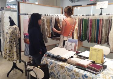 Two women browsing fabric samples at a market stall.