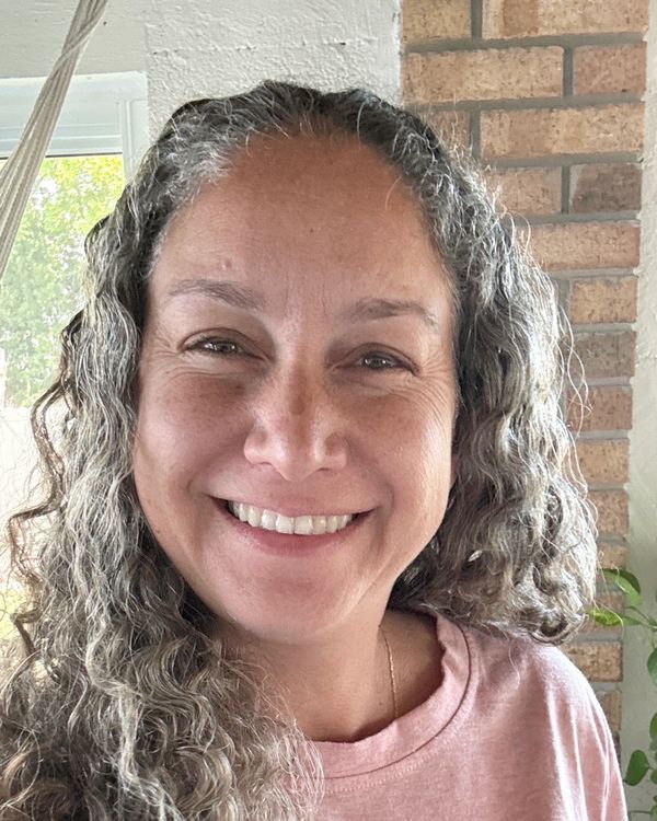 Smiling woman with curly gray hair in a cozy indoor setting.