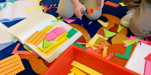 Children crafting with colorful paper shapes and glue on a carpeted floor.