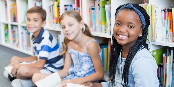 Three kids reading books in a library.