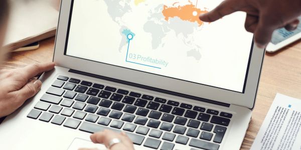 People analyzing profitability data on a laptop world map.