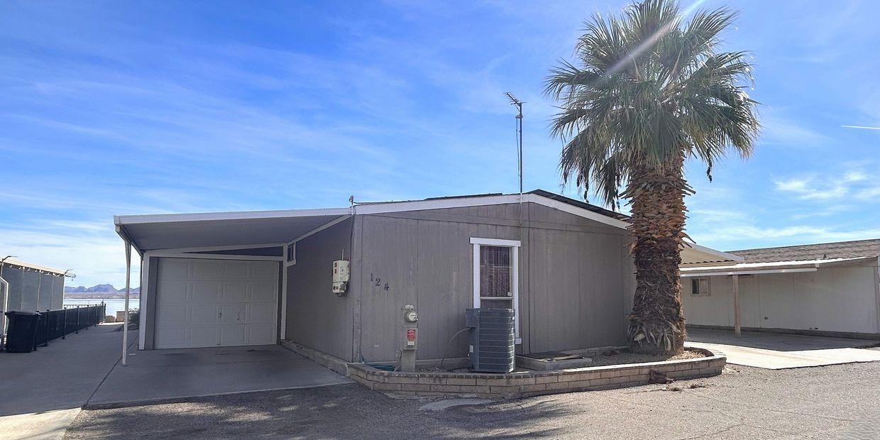 Single-story house with a palm tree and carport under clear blue sky.