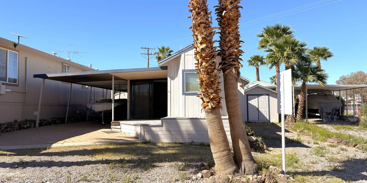 A small house with a carport and palm trees under a clear blue sky.