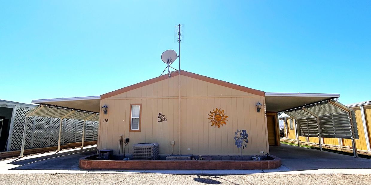 Mobile home with dual carports and decorative wall art under a clear sky.