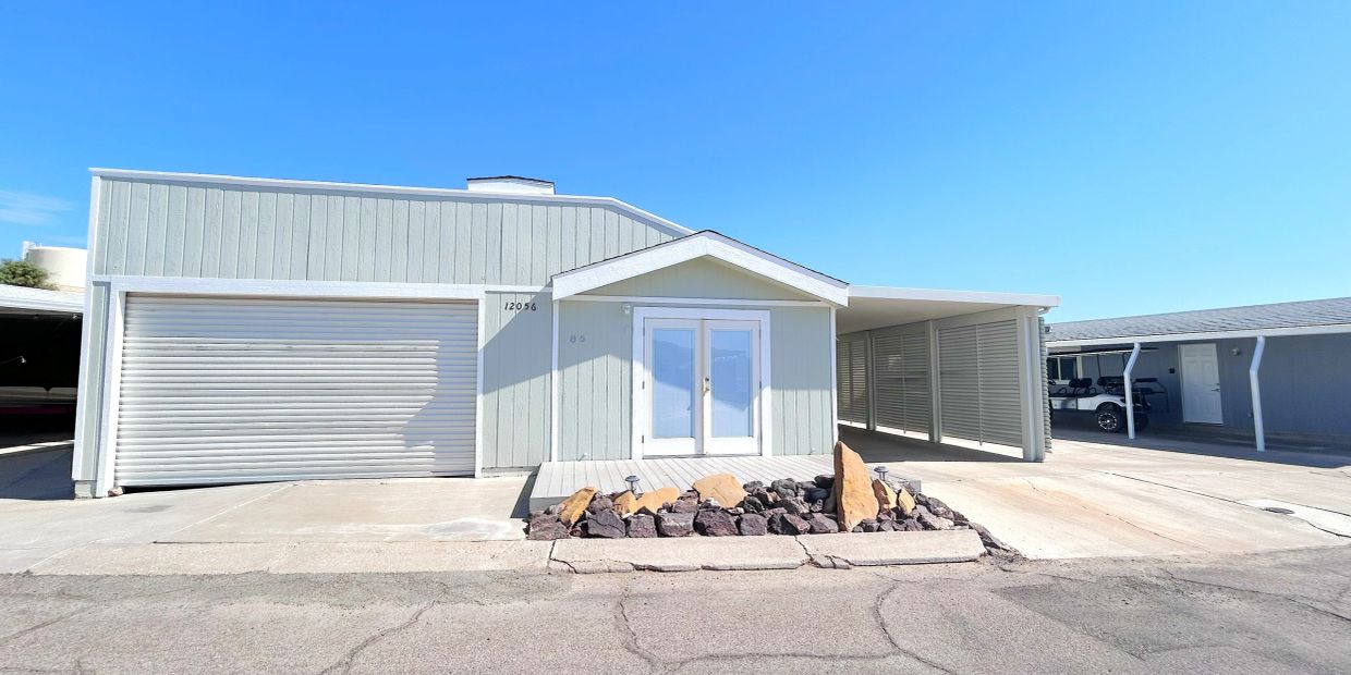 Modern light gray house with garage and carport under clear blue sky.