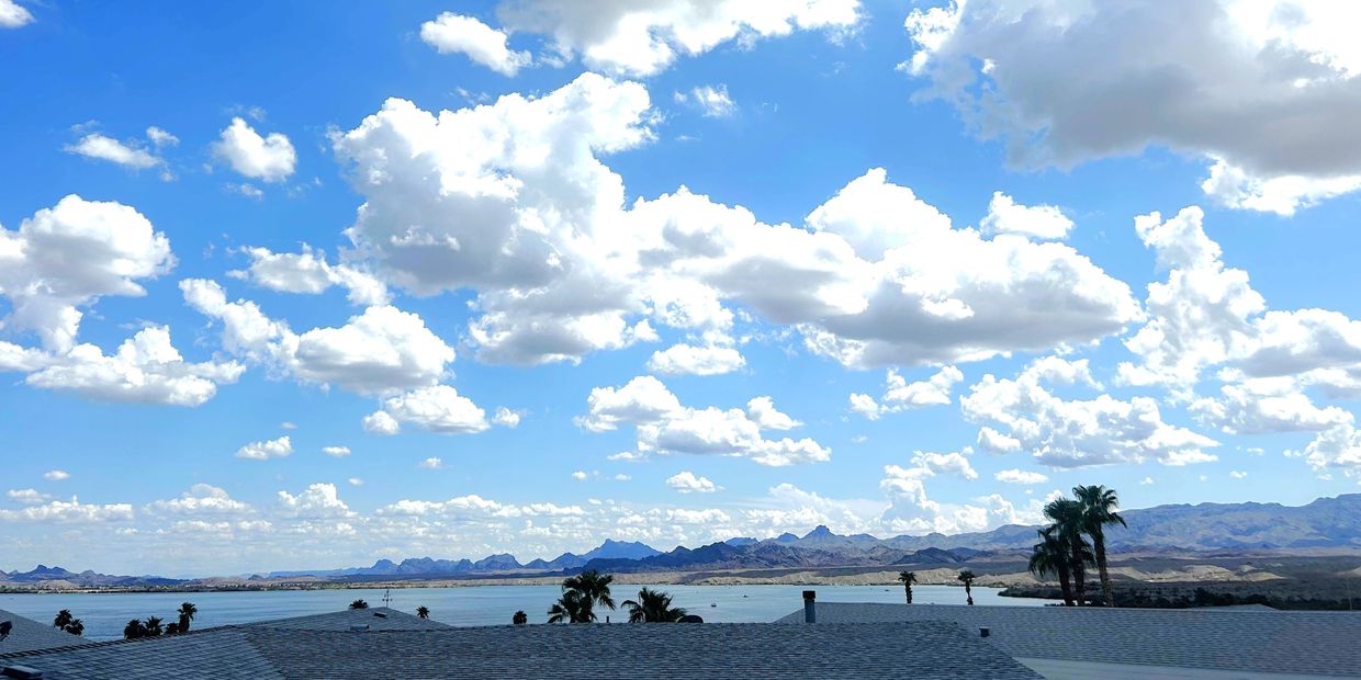 Clouds scattered over a lake with mountains and rooftops in the foreground.