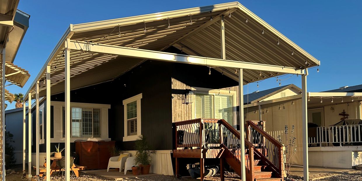 A cozy porch with wooden stairs and chairs under a metal roof on a sunny day.