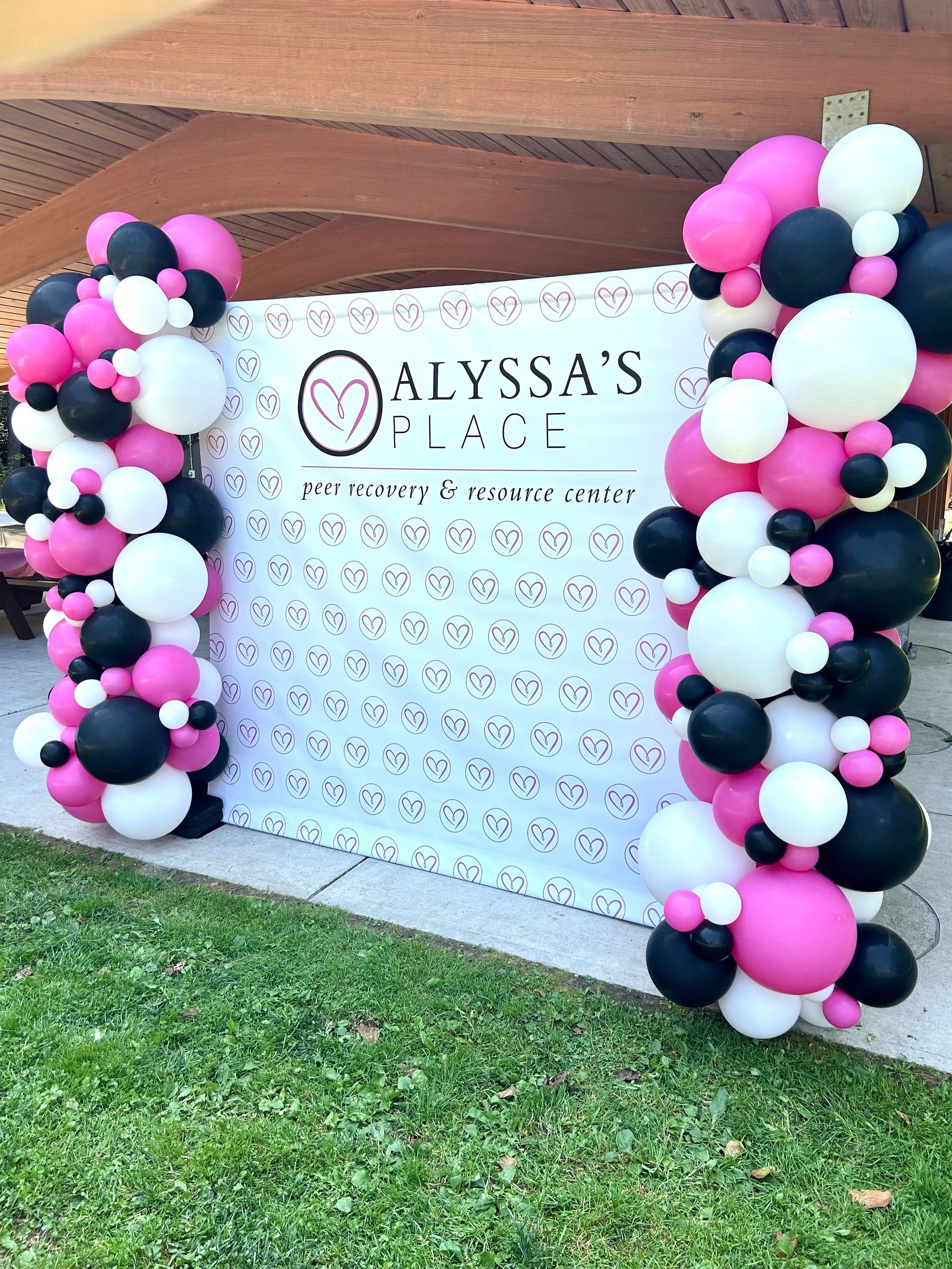 A colorful balloon arch frames Alyssa's Place banner at a peer recovery event.