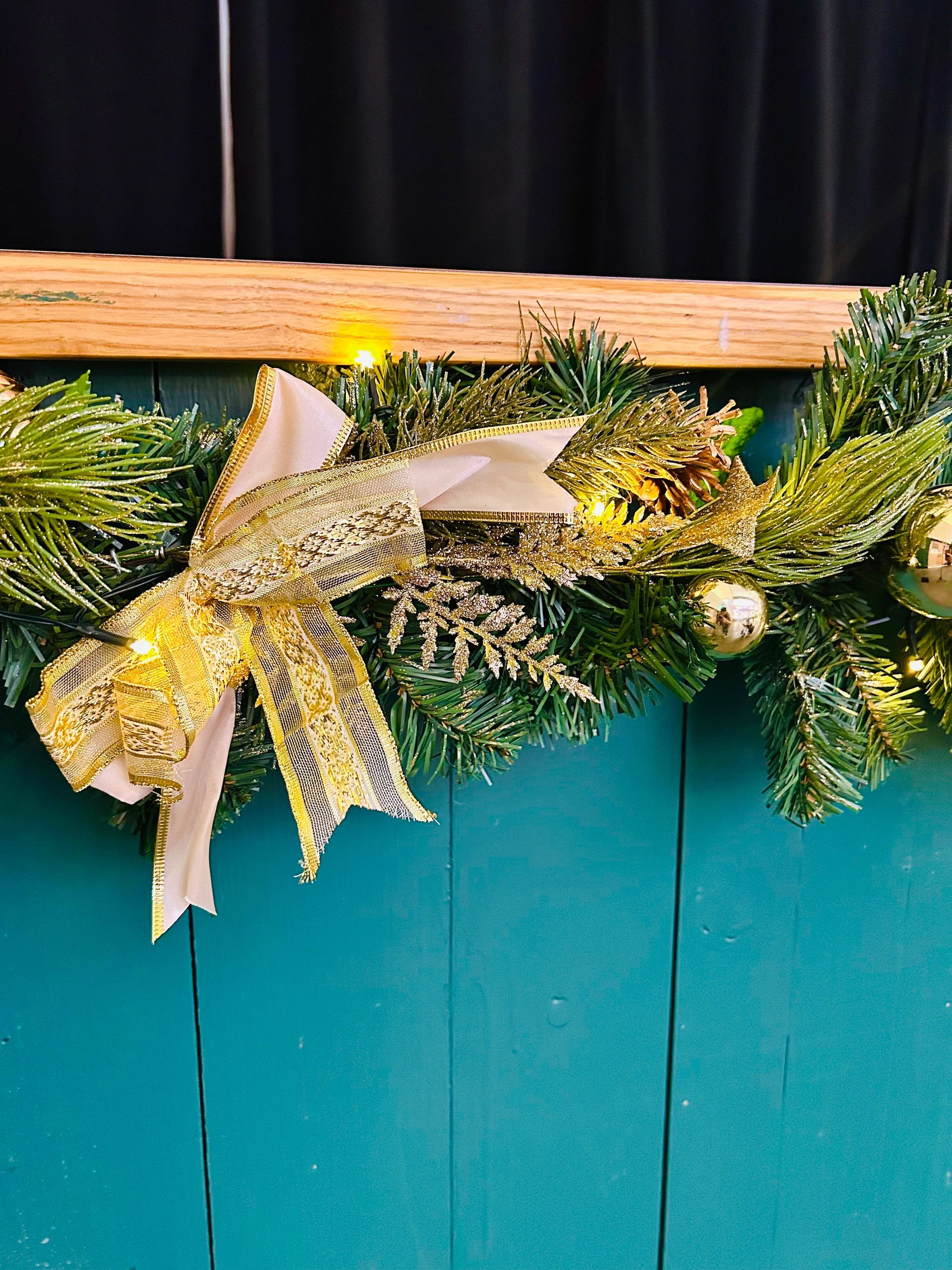 Festive Christmas wreath with a gold ribbon and pine decorations on a teal door.