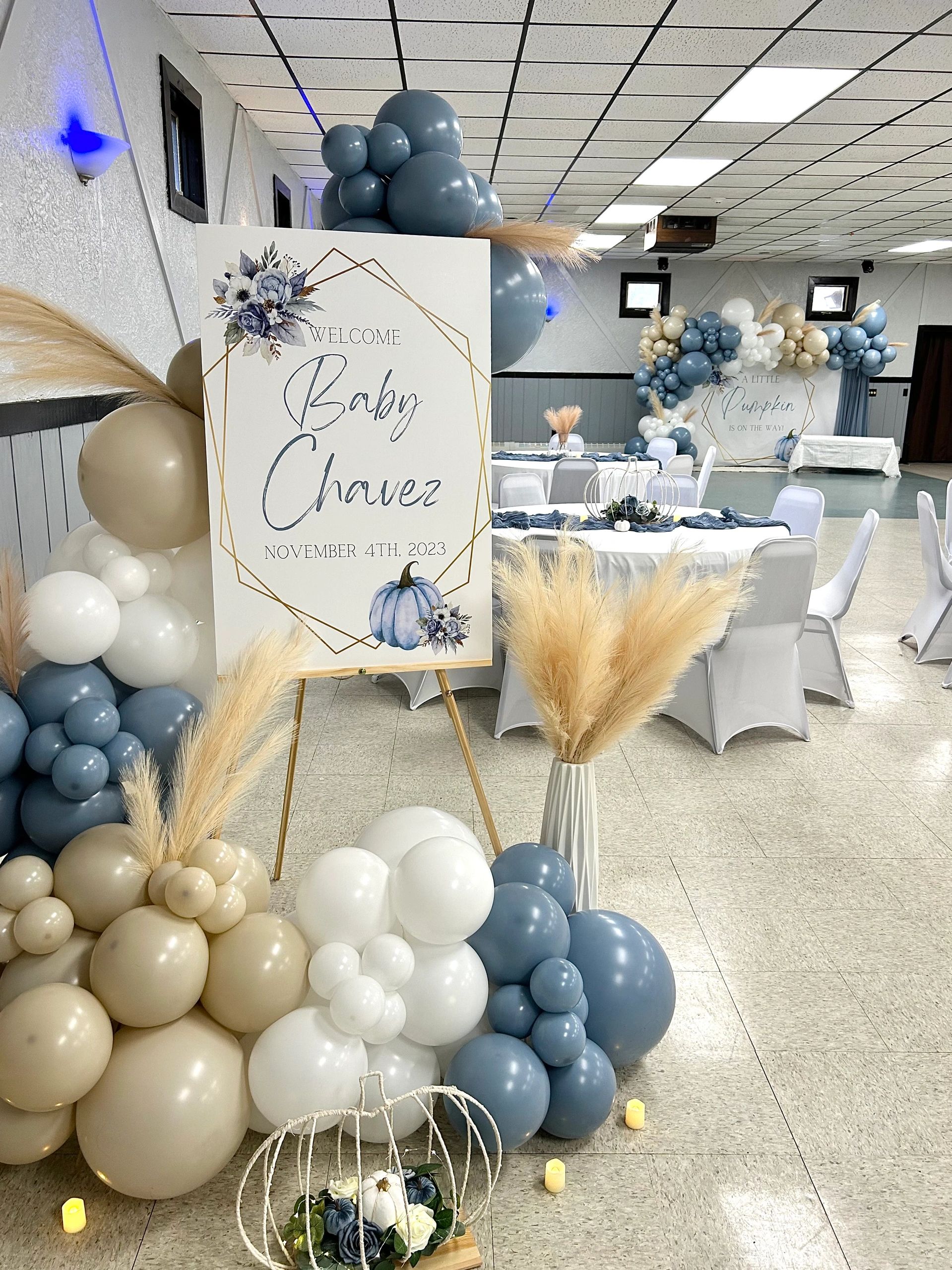 Elegant baby shower setup with blue, white, and beige balloons and floral decor.