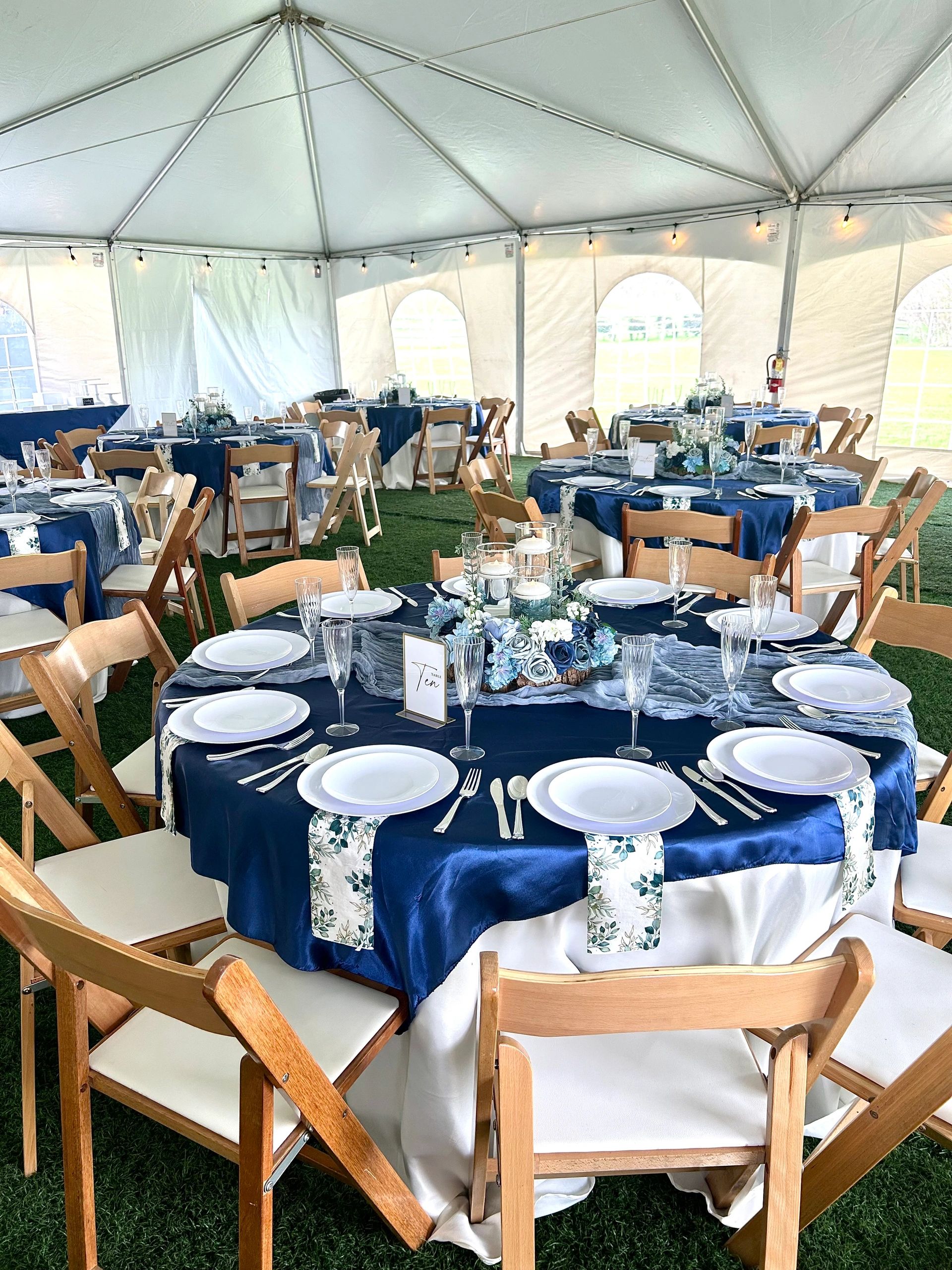 Elegantly decorated event tables with navy blue and floral accents inside a white tent.