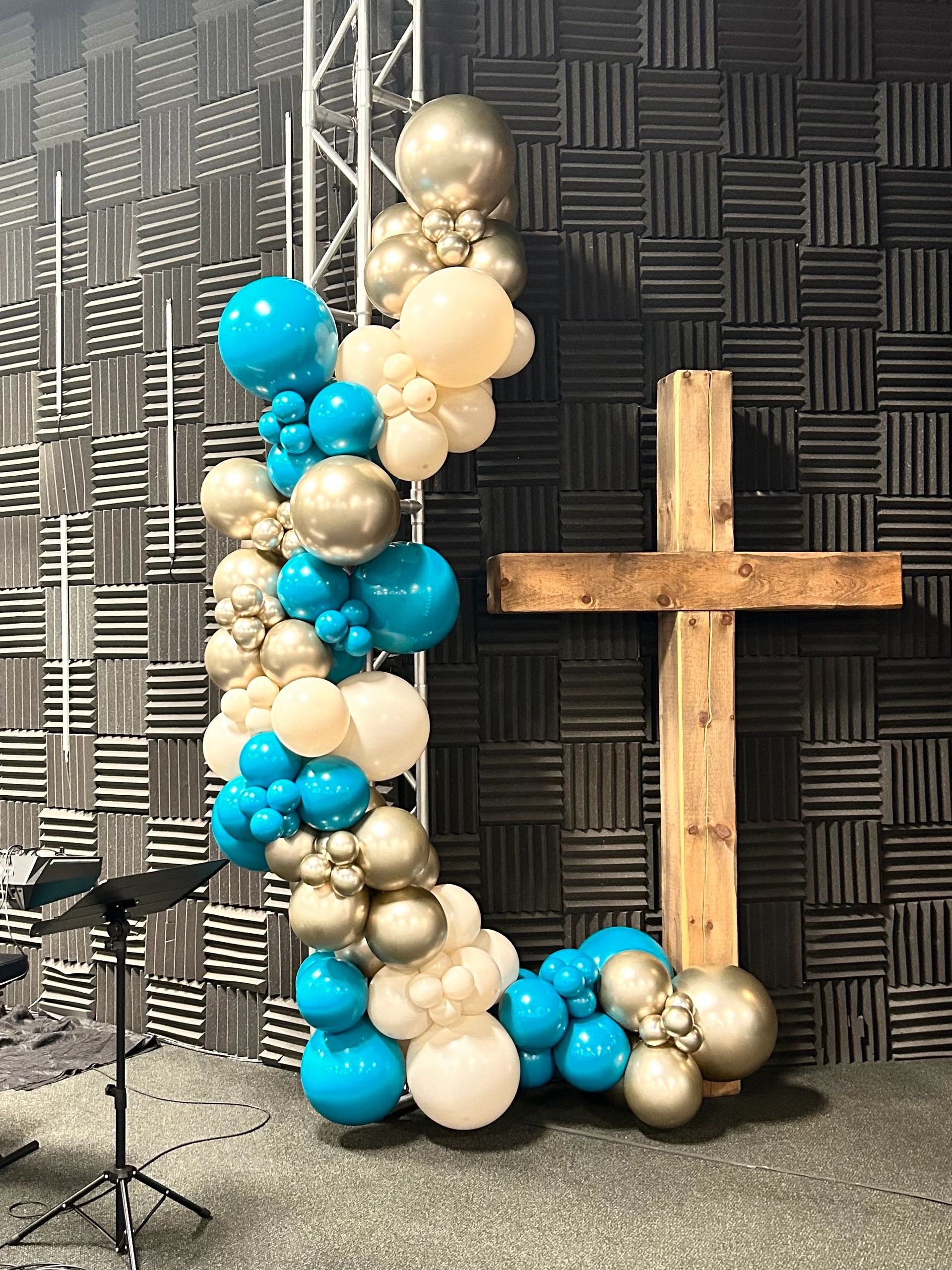 Colorful balloon arch next to a wooden cross in a soundproof room.