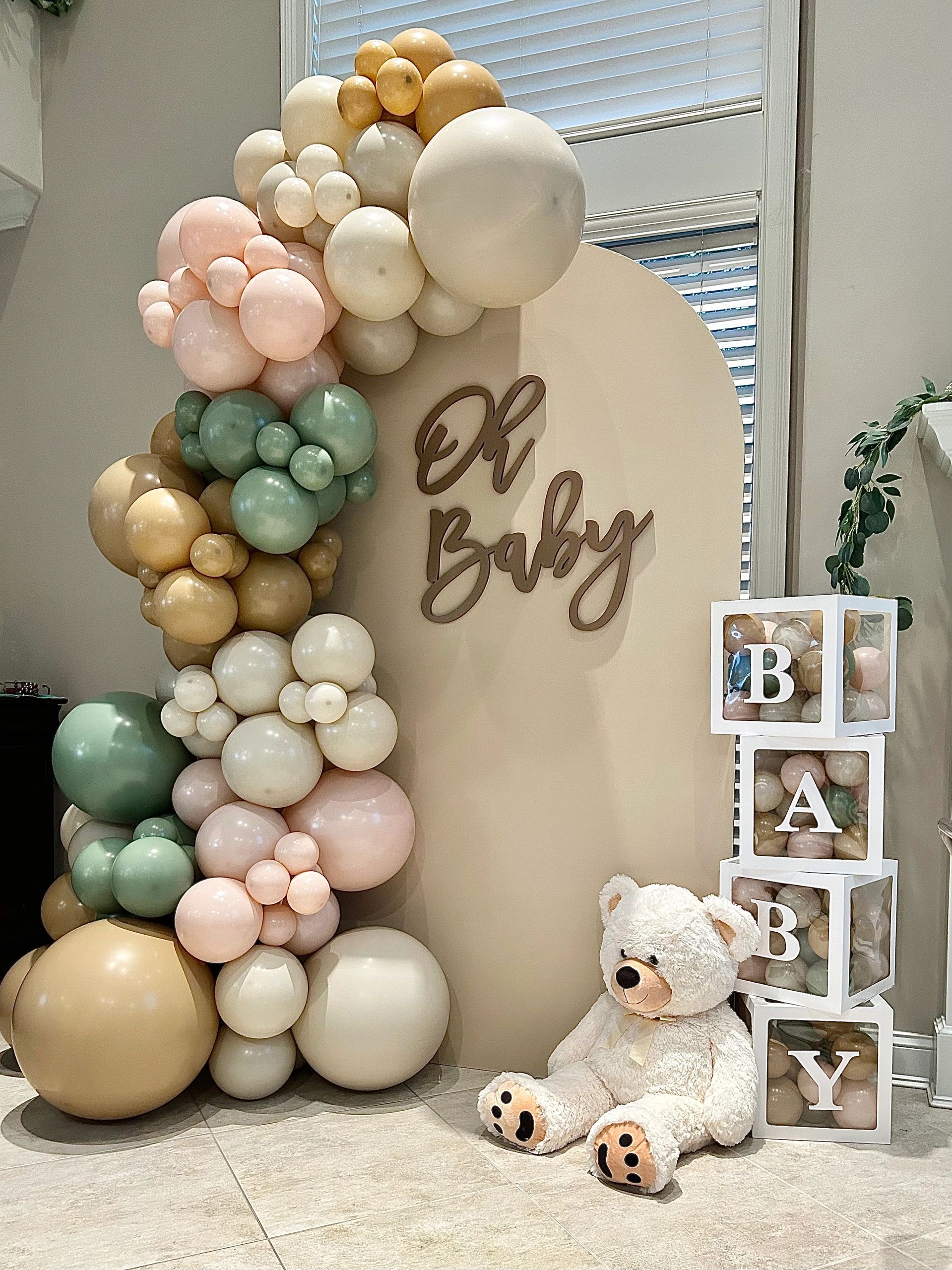 Neutral-toned balloon arch and teddy bear at baby shower setup.