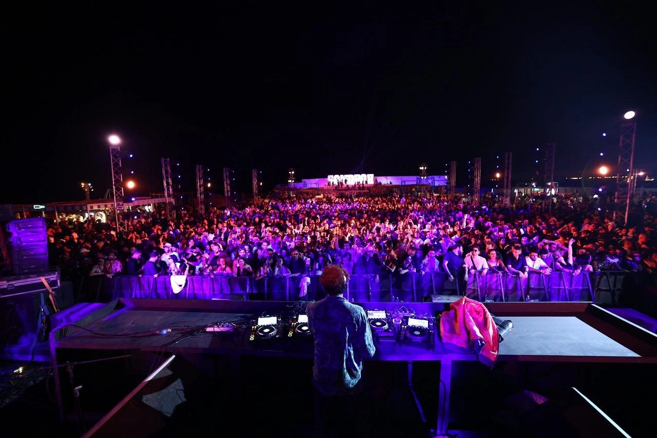 Sandbox Festival at night in El Gouna — a DJ playing to a packed crowd under the illuminated Sandbox sign