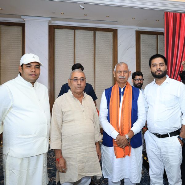 A group of men posing indoors at a formal event with a woman in traditional attire in the background.