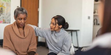 A woman comforts another woman who looks upset indoors.