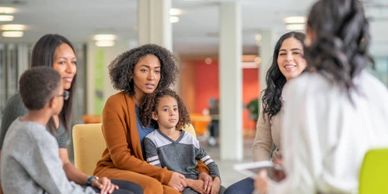 A group of diverse women and children engaged in a supportive group discussion.