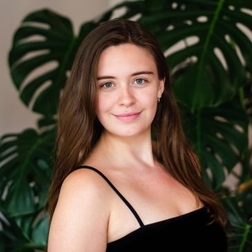 Young woman smiling in front of large green leaves.
