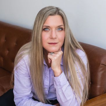Woman with long blonde hair sitting on a brown leather couch, resting her chin on her hand.