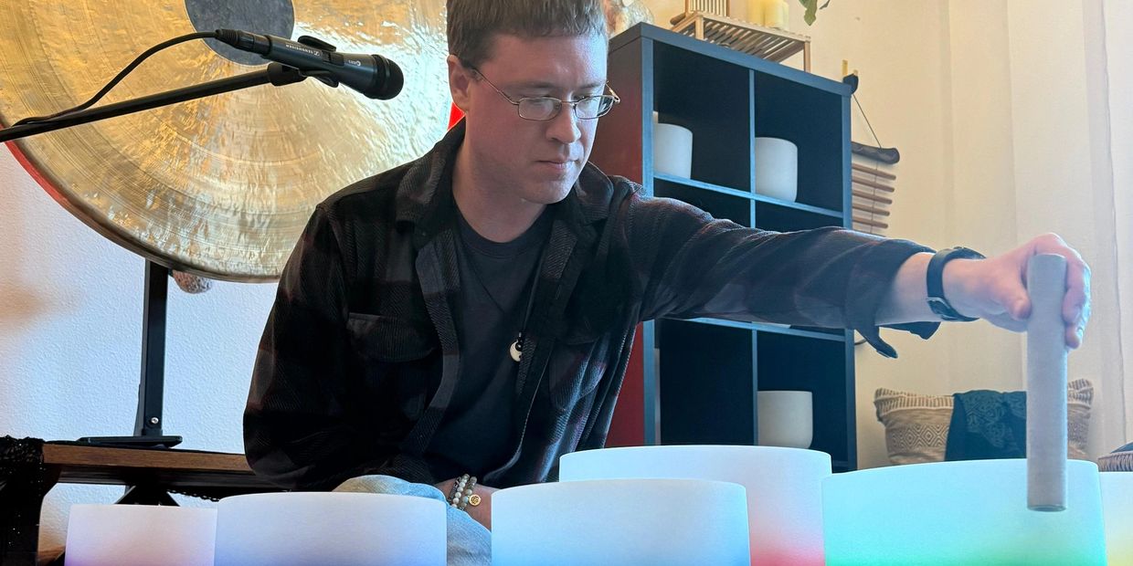 Man playing crystal singing bowls in a serene room with a gong and microphone.