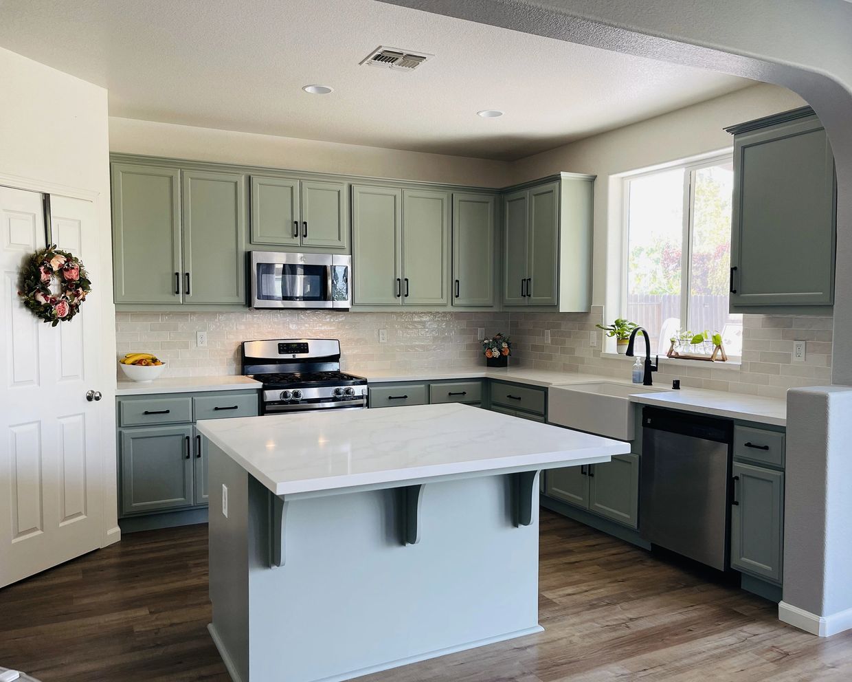 Remodeled kitchen with sage green cabinets, quartz island, farmhouse sink, and subway tile backsplas