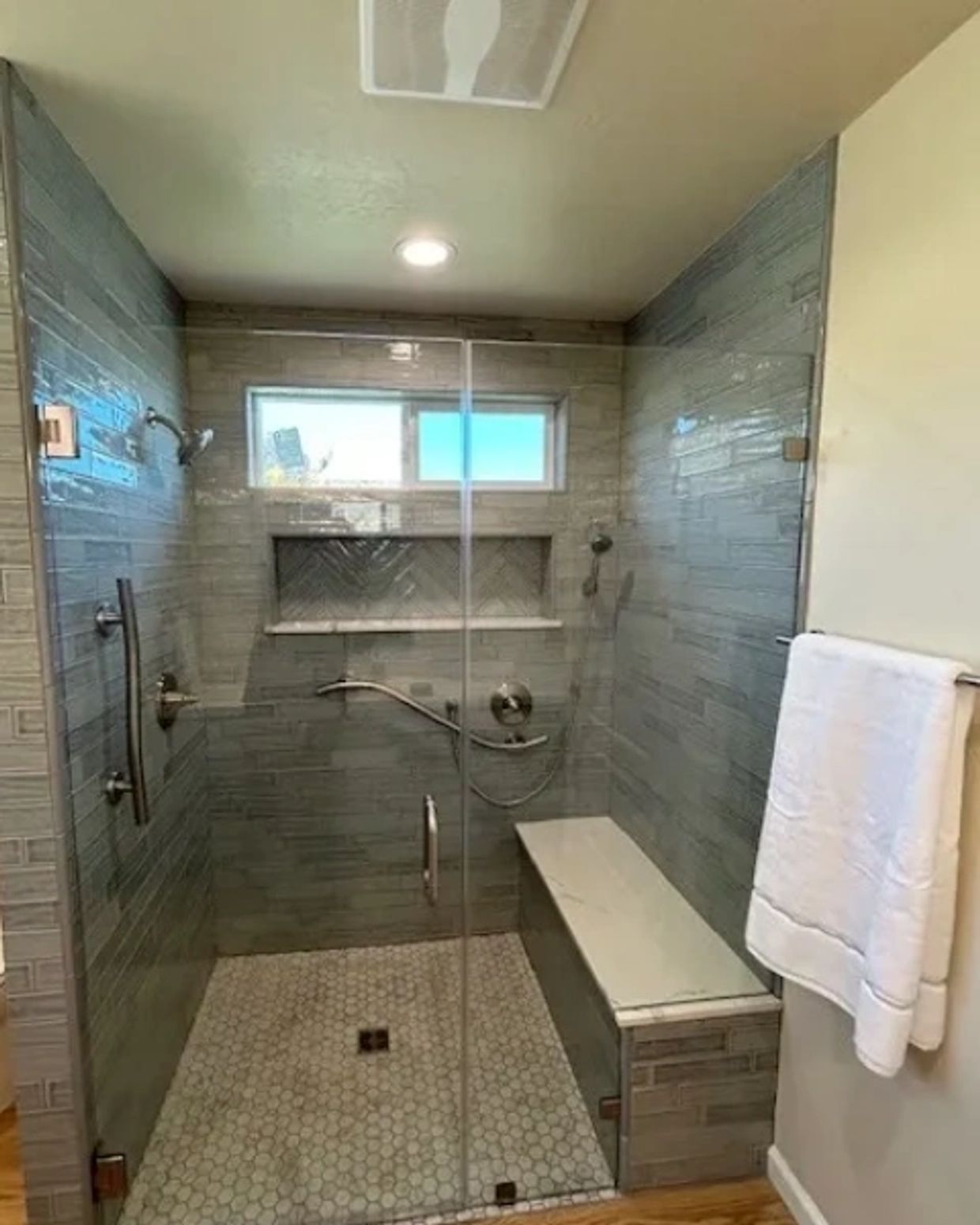 Custom Tile curbless walk-in shower with frameless glass door and full-length bench seating. 