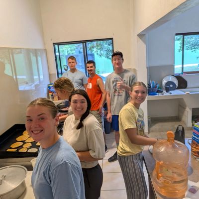Group cooking pancakes in a bright kitchen.