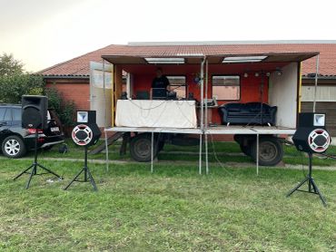Outdoor DJ setup inside a truck with speakers on stands in front.