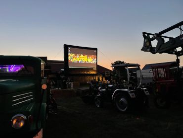 Outdoor movie screening at dusk with tractors parked nearby.
