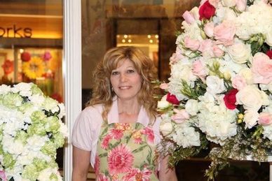 A florist stands among large, colorful flower arrangements inside a shop.