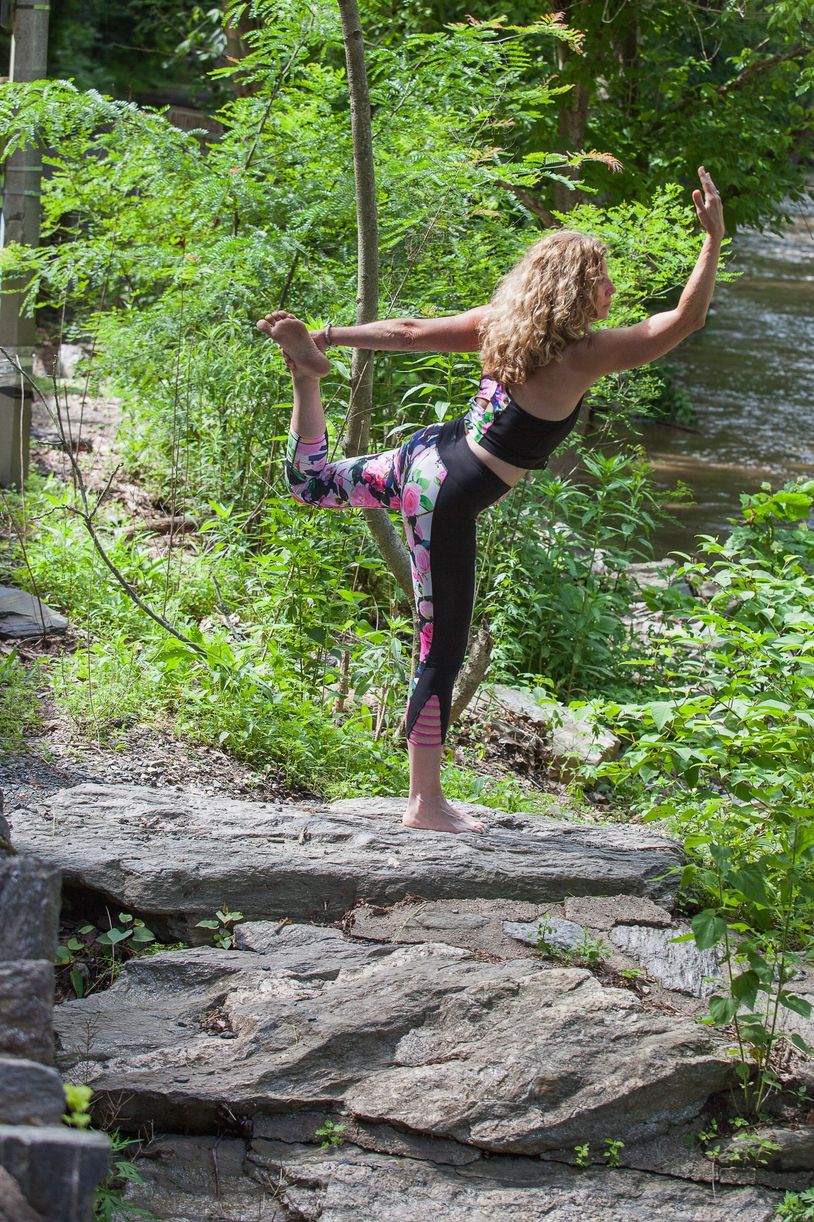 Woman practicing yoga outdoors near a river, balancing on one leg.