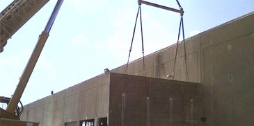 Crane lifting large concrete wall section.