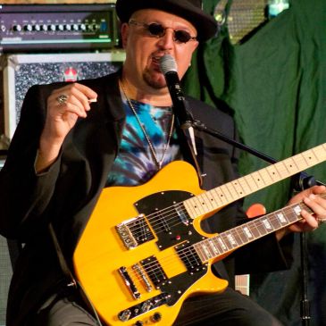Musician playing a double-neck electric guitar and singing into a microphone.