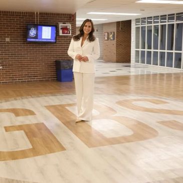 A woman in a white suit stands on a floor with large letters in a modern building.
