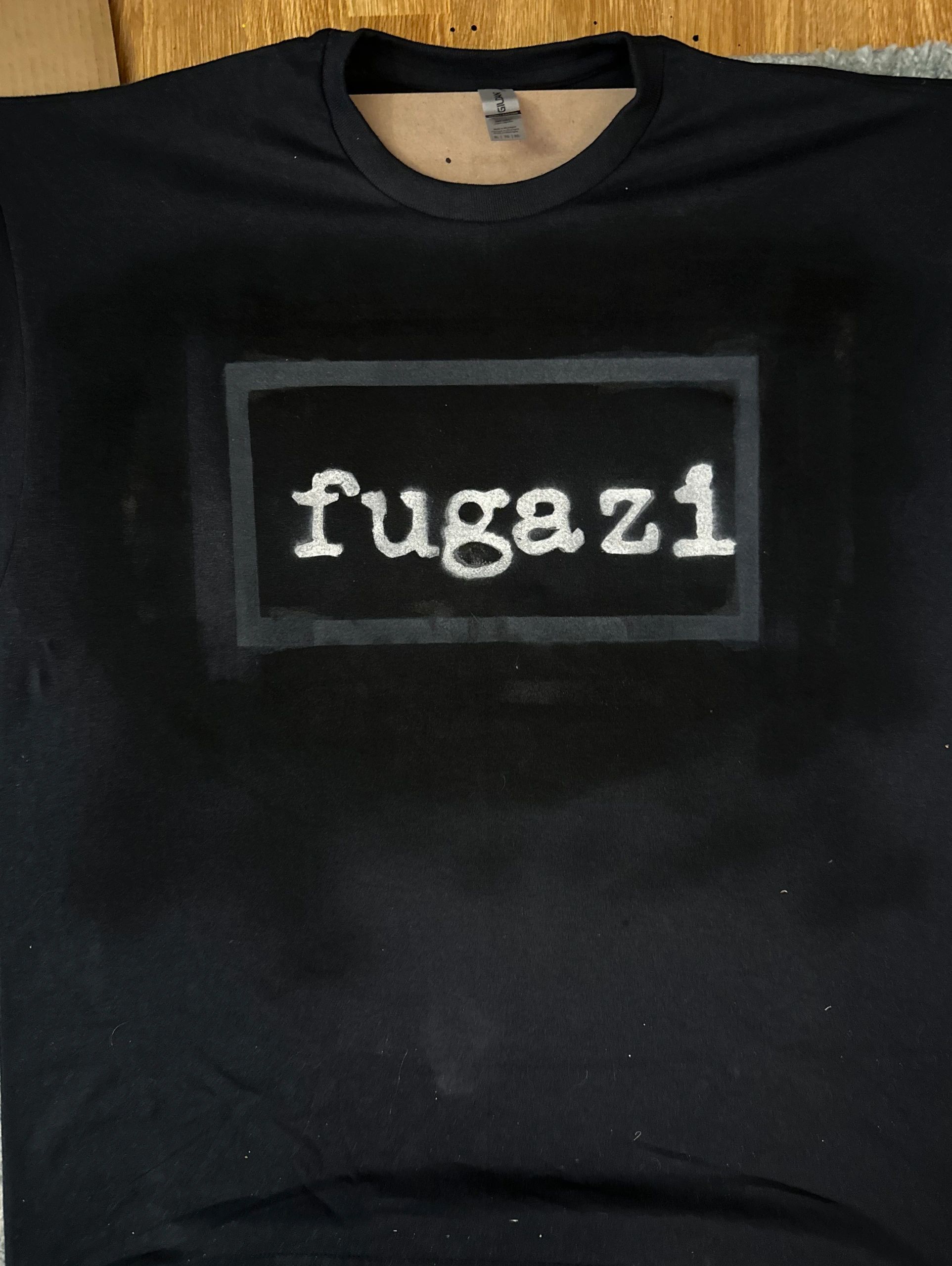 Black t-shirt with white 'fugazi' text in a rectangle.