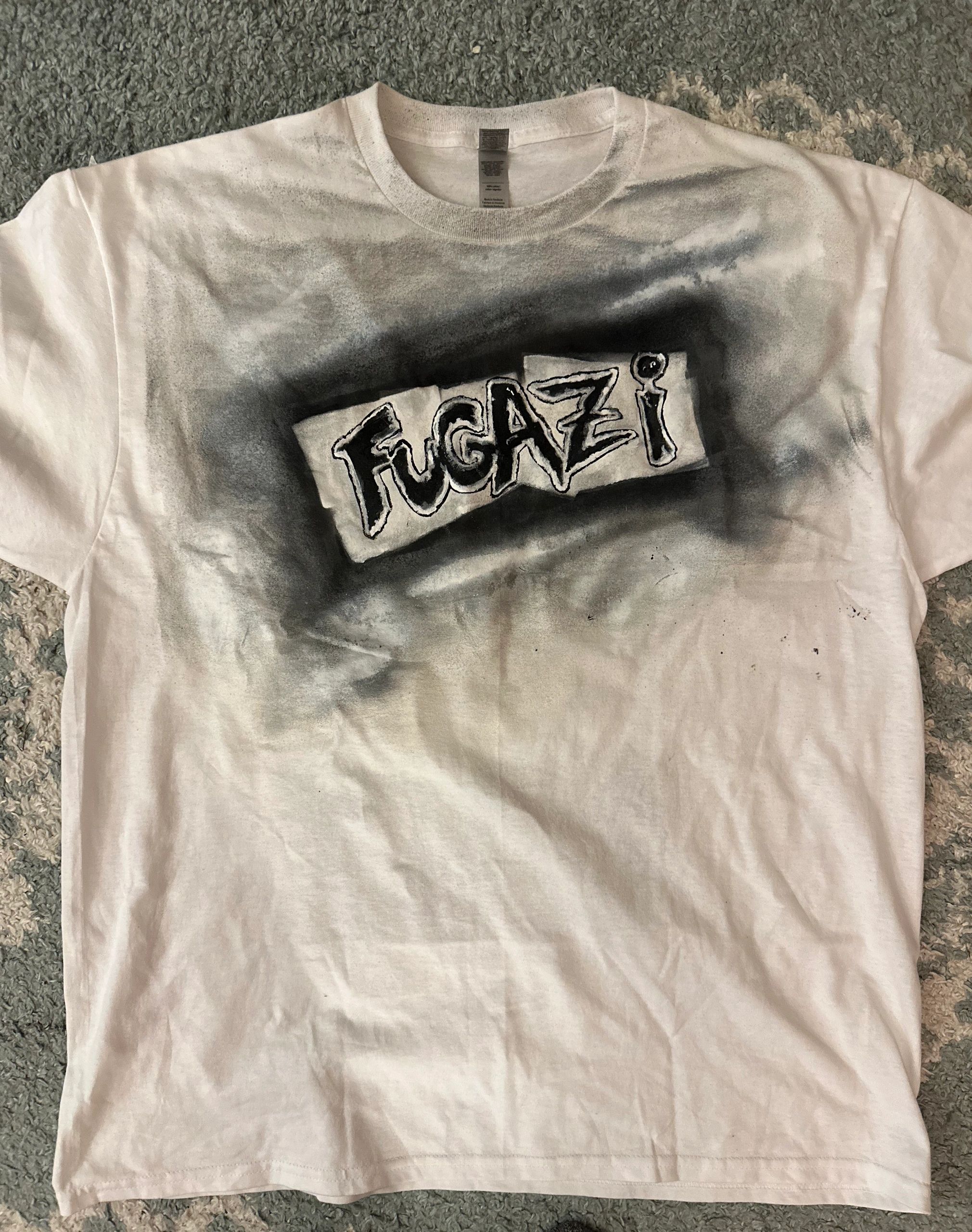 White T-shirt with black airbrushed Fugazi logo.